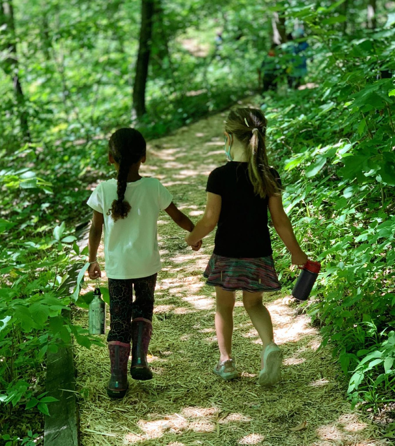 two children holding hands while walking on a forest trail
